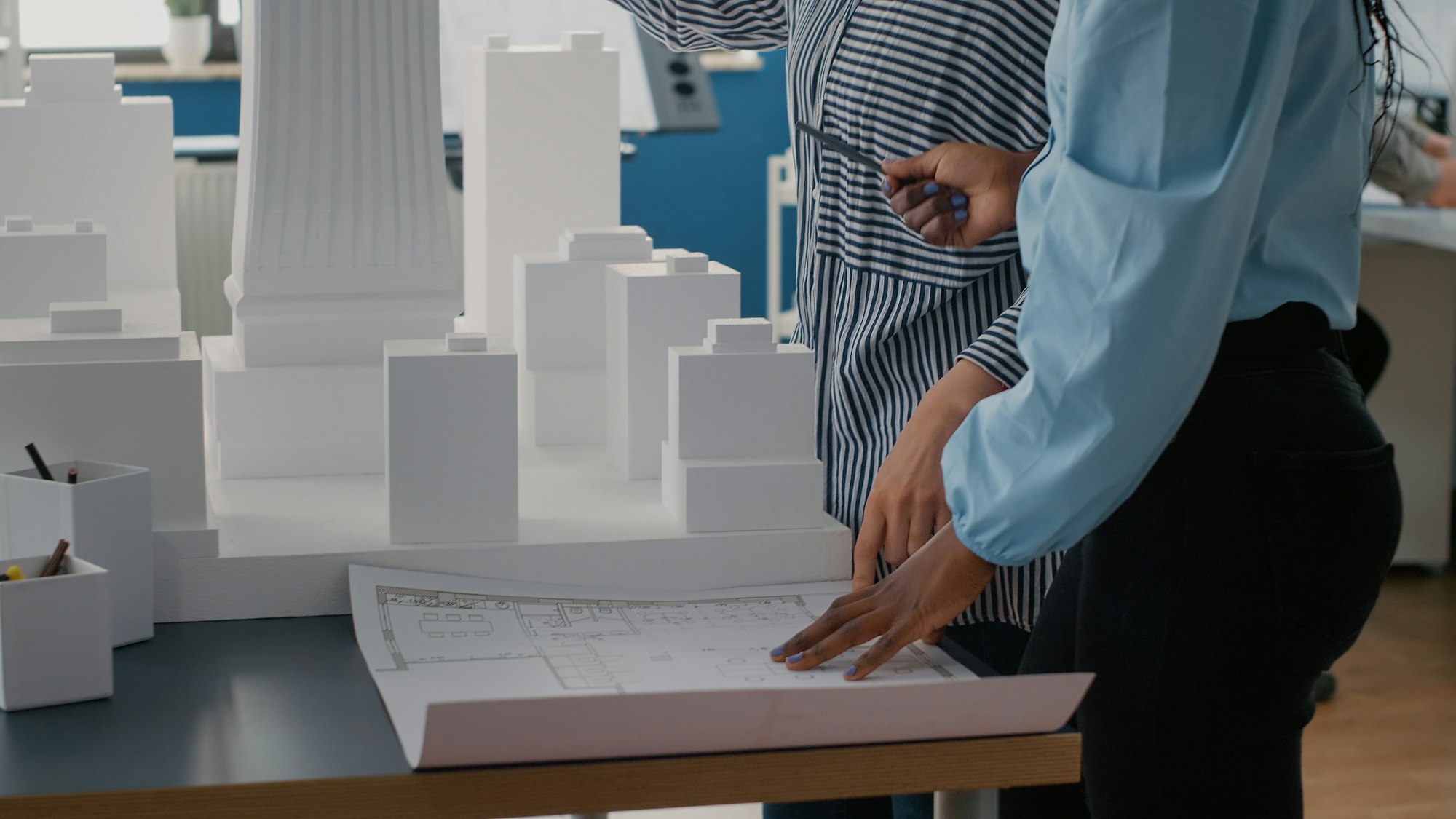 Close up of architects placing blueprints plan on table to work on urban project with building model